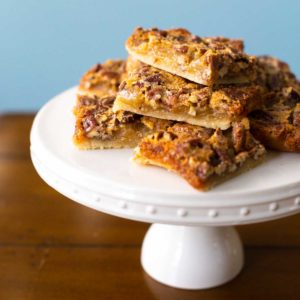 A stack of shortbread pecan pie bars on a cake plate for serving.