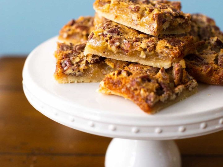 A stack of shortbread pecan pie bars on a cake plate for serving.