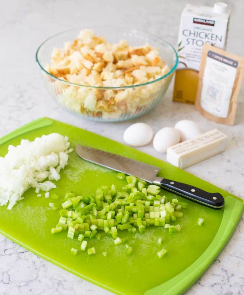 Prepped celery and onions are on a chopping board next to the rest of the stuffing ingredients.