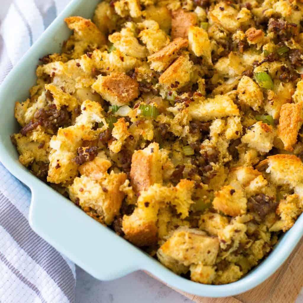 A baking dish filled with homemade Italian sausage stuffing sits next to a striped towel.