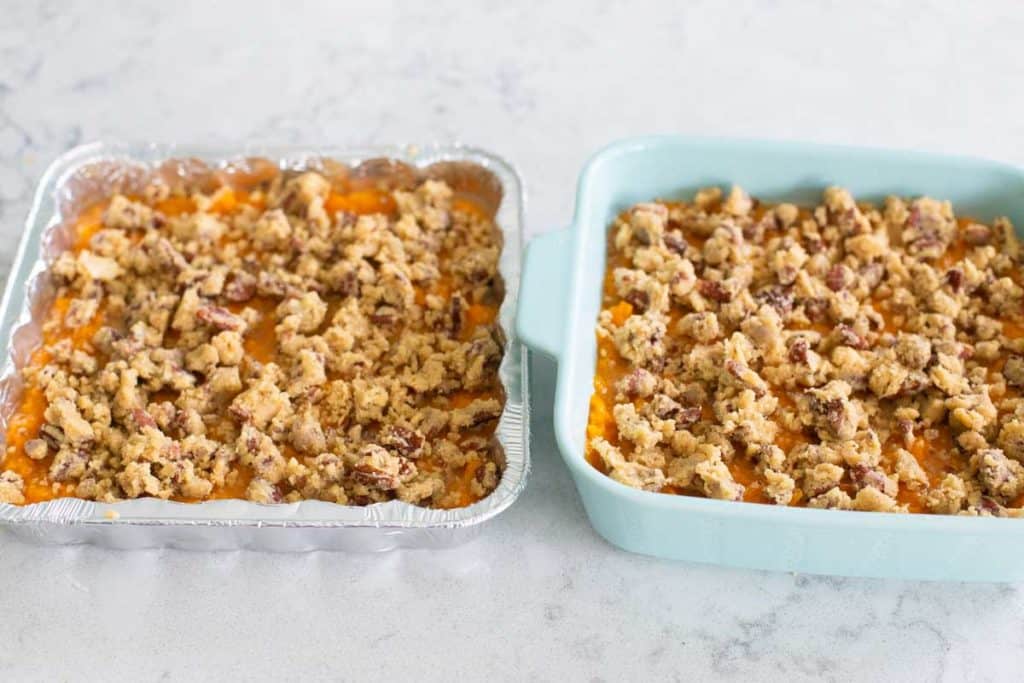 Two pans of sweet potato casserole have the pecan topping spread over the top.