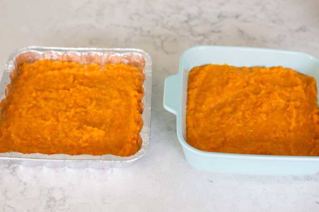 Two square pans have a layer of mashed sweet potato casserole filling spread evenly.