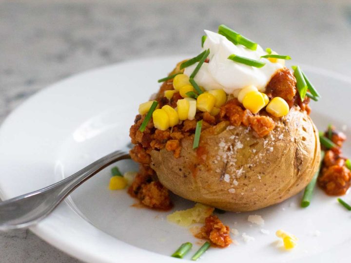 A baked potato is stuffed with crockpot chicken taco chili and then topped with corn and a dollop of sour cream.