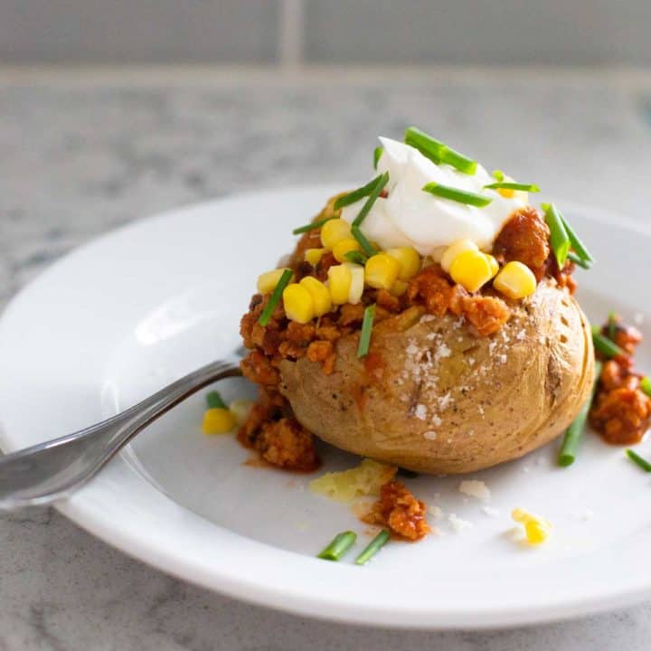 A baked potato is stuffed with crockpot chicken taco chili and then topped with corn and a dollop of sour cream.