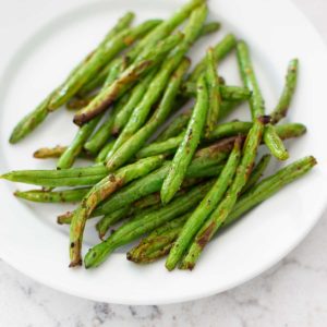 A white plate has a pile of freshly roasted green beans hot from the air fryer basket.