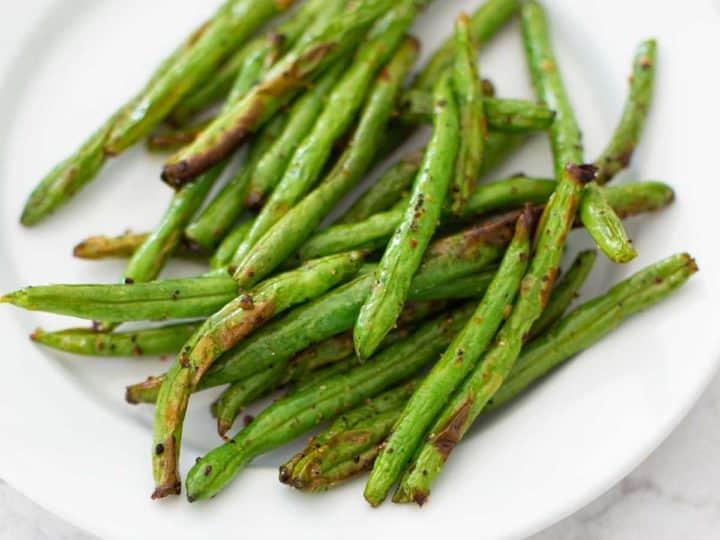 A white plate has a pile of freshly roasted green beans hot from the air fryer basket.