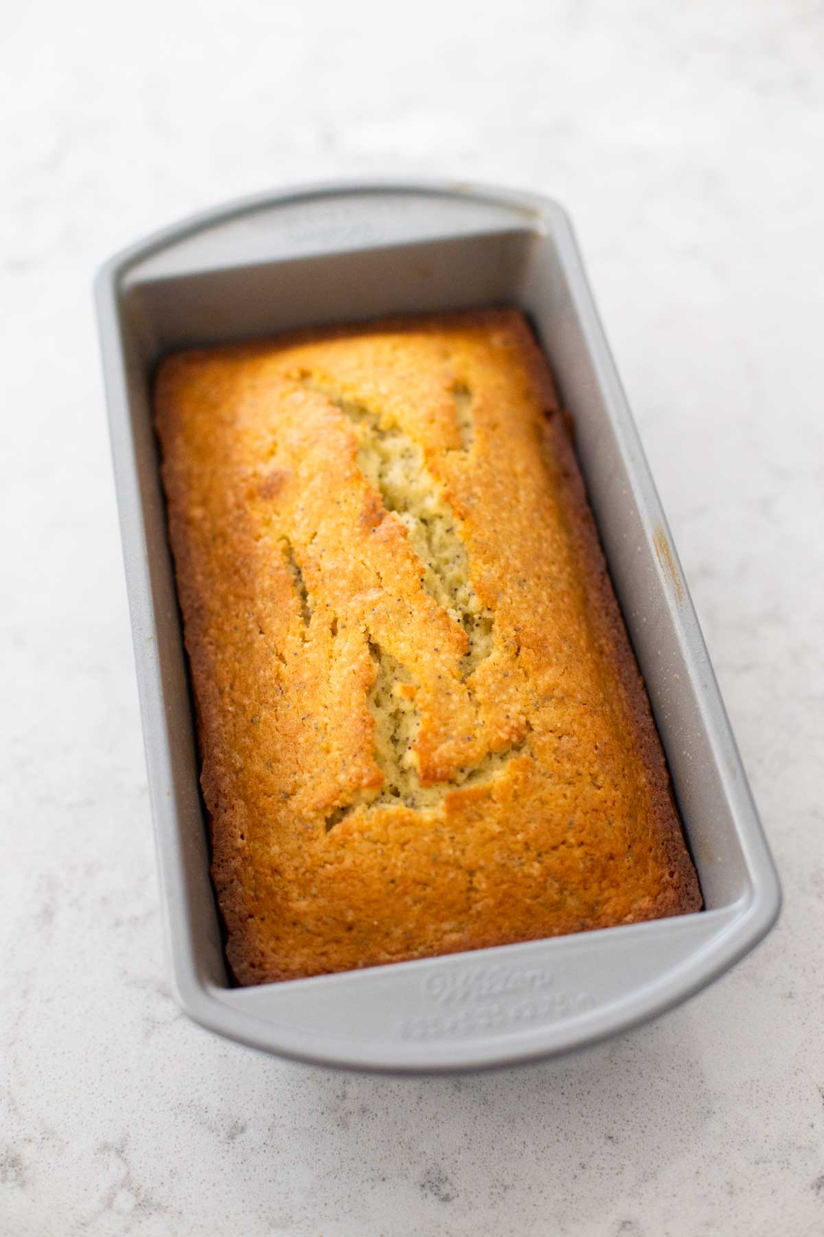 The baked almond poppy seed bread in the bread pan shows how the crust should look when it is done.