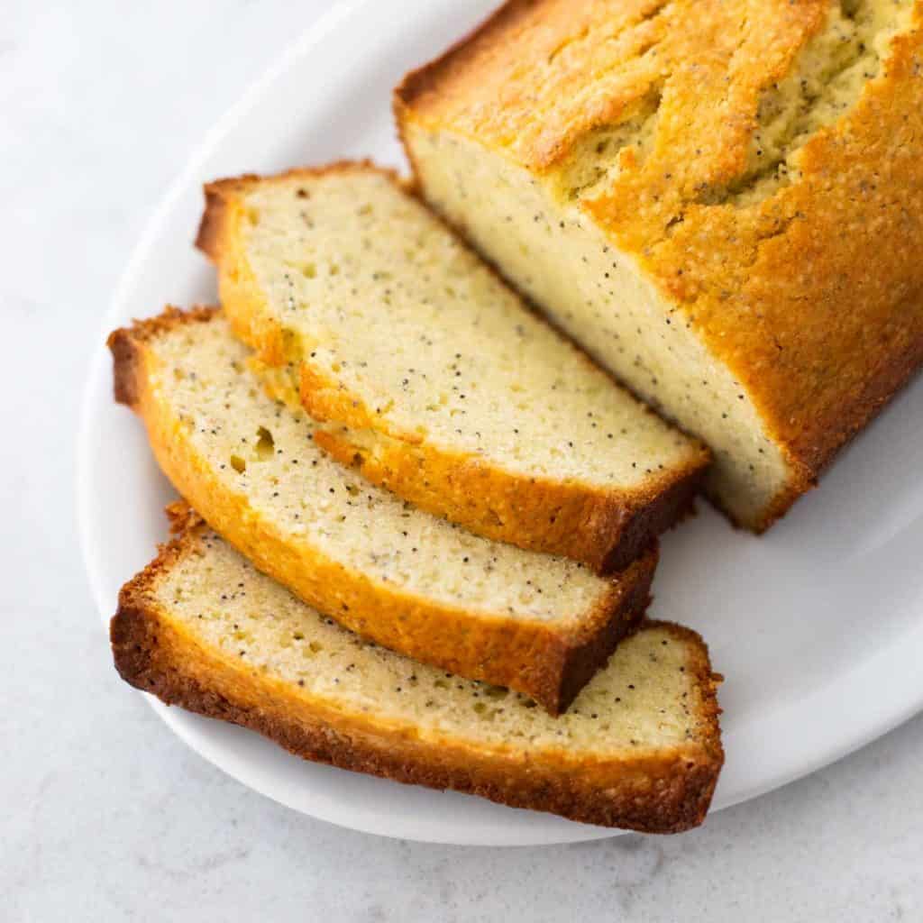 A sliced loaf of almond poppy seed bread is ready for serving on a white platter.