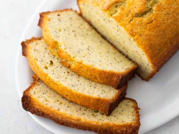 A sliced loaf of almond poppy seed bread is ready for serving on a white platter.