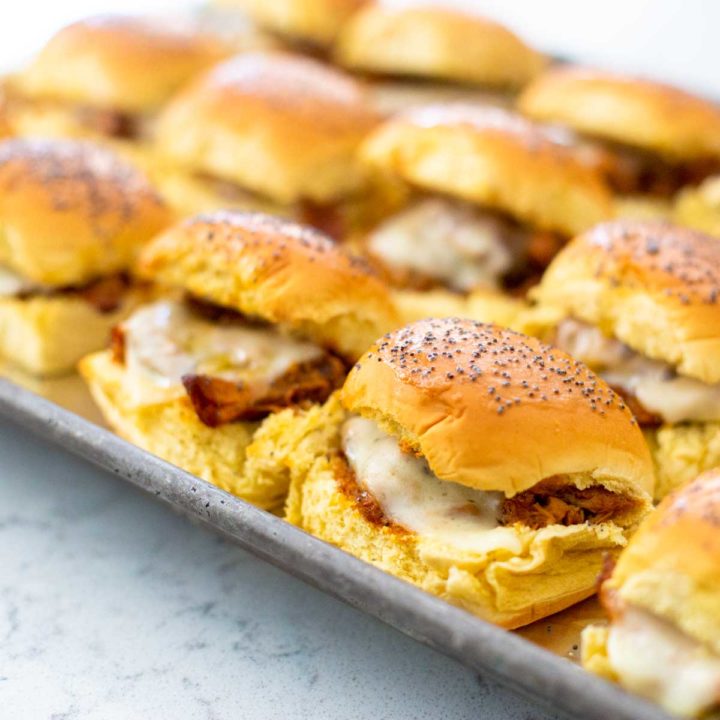 A metal baking pan has 3 rows of baked bbq chicken sliders showing the melted cheese oozing out.