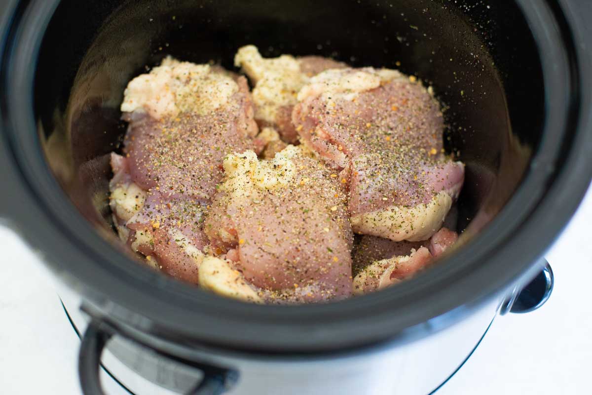 Seasoned chicken thighs are layered in a Crockpot.