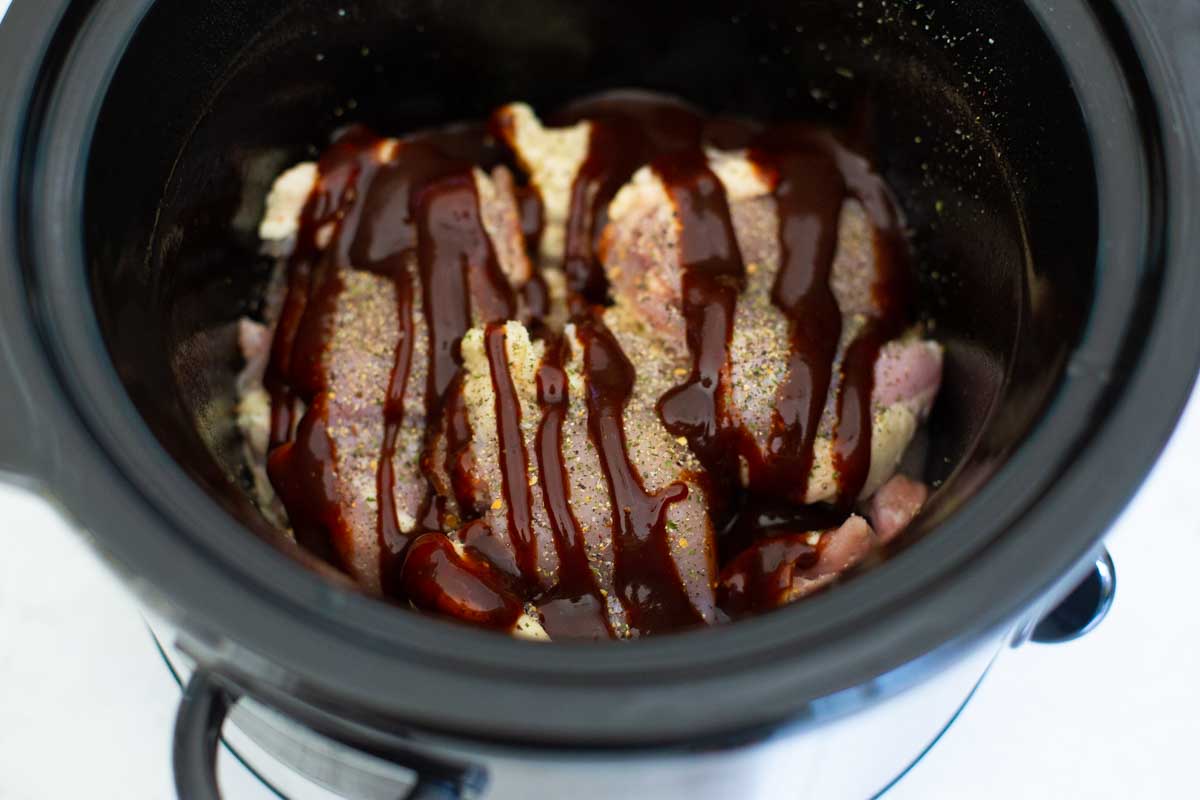 BBQ sauce has been drizzled over the chicken thighs in the slowcooker.