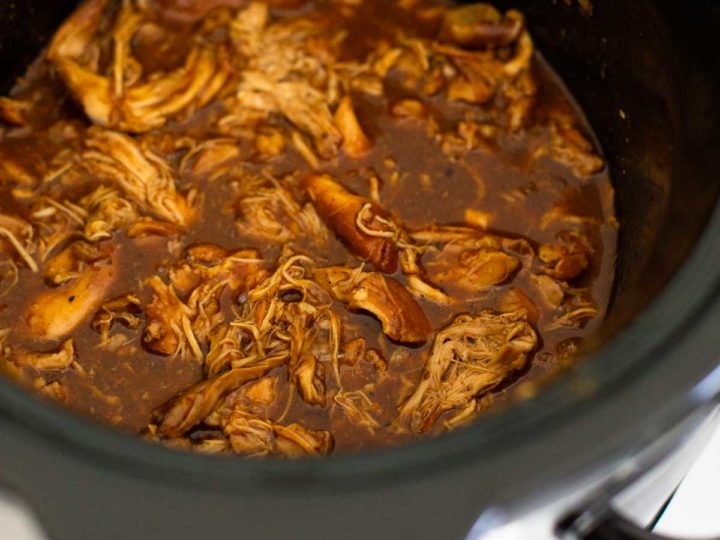 A Crockpot is filled with shredded bbq chicken thighs and bbq sauce.