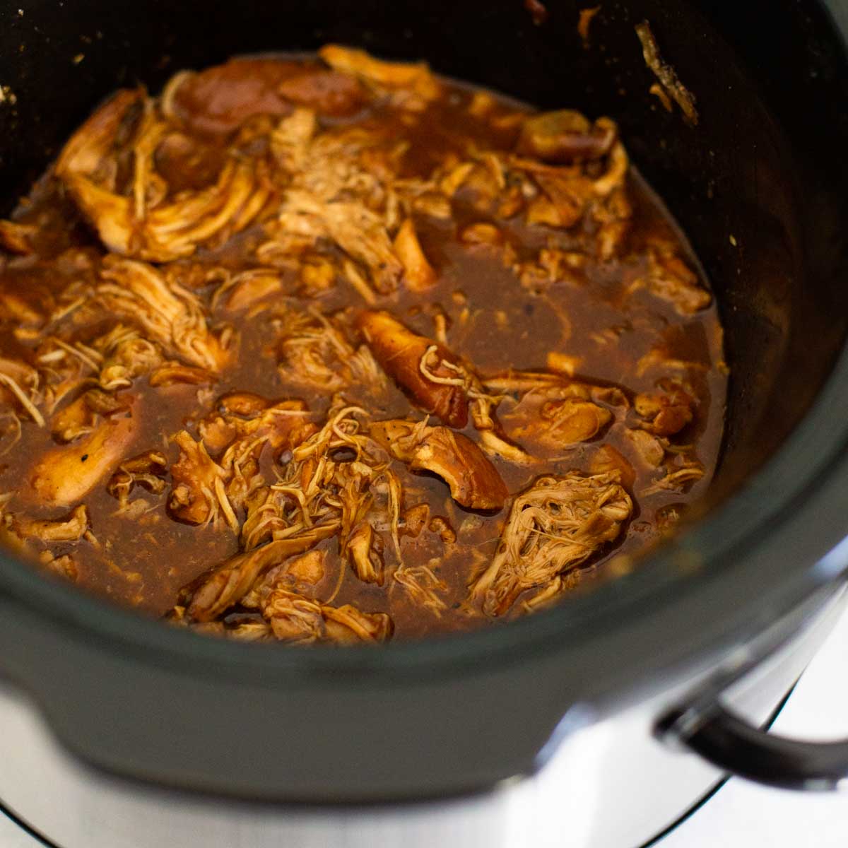 A Crockpot is filled with shredded bbq chicken thighs and bbq sauce.