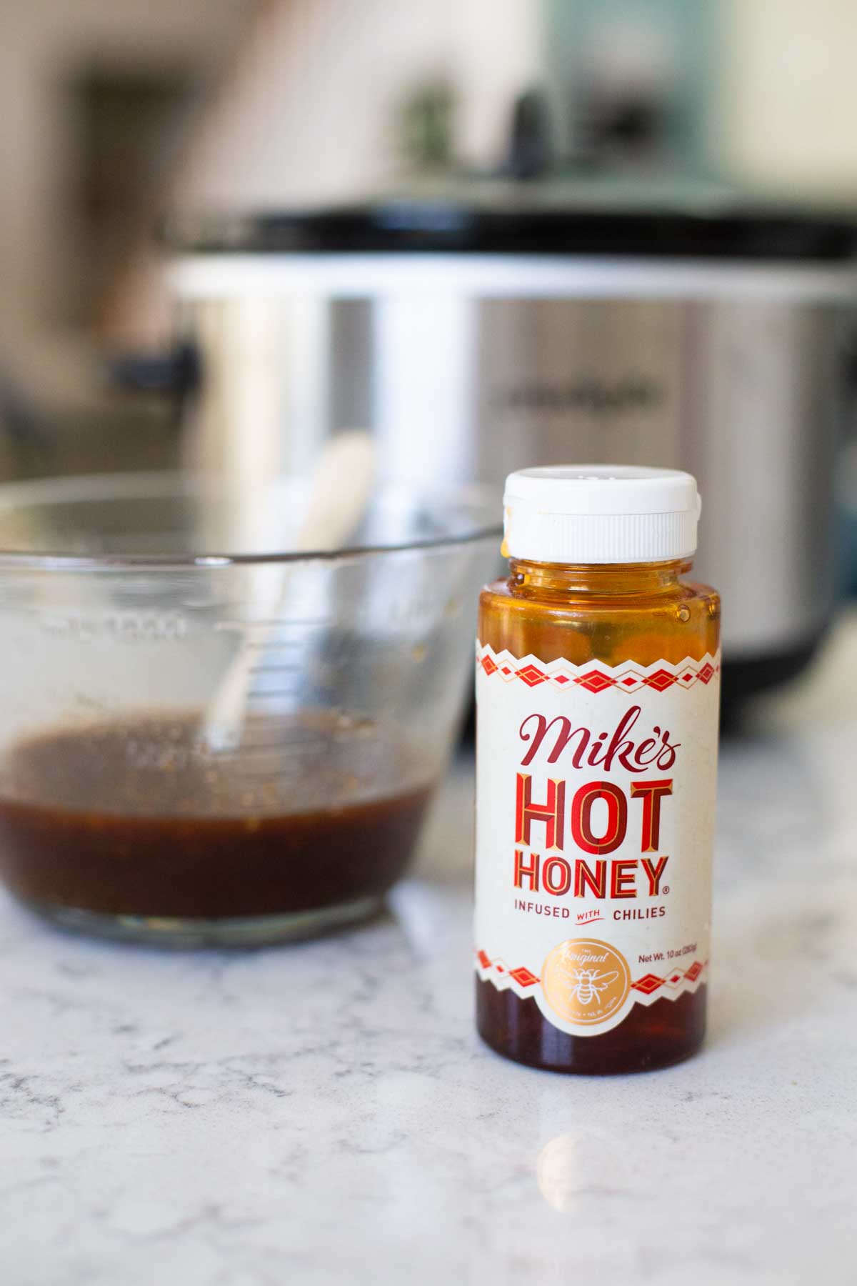 A jar of Mike's Hot Honey sits in front of a measuring cup filled with chicken marinade.