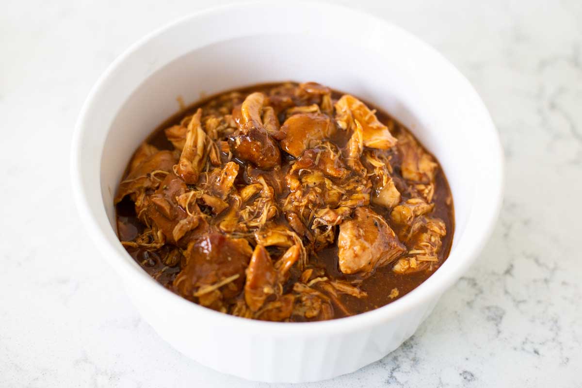 A white storage dish has shredded bourbon chicken ready to be kept in the fridge.