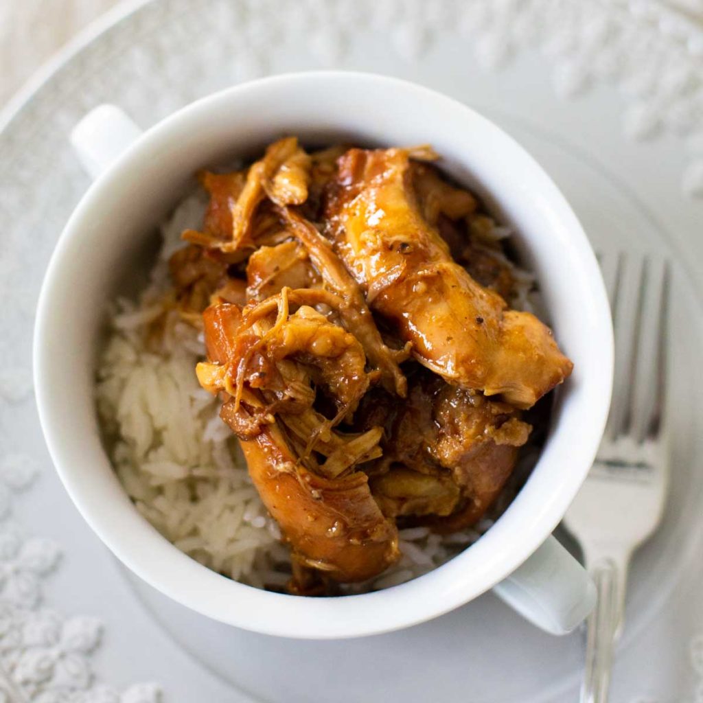 A bowl of rice is topped with shredded bourbon chicken from the crockpot.