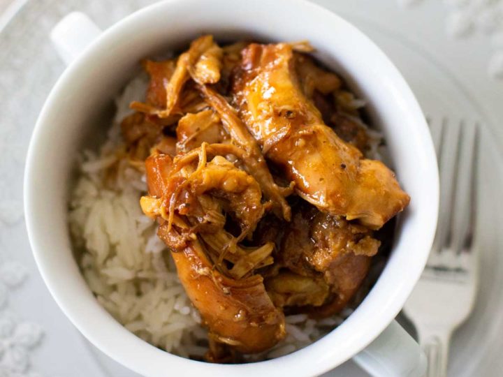A bowl of rice is topped with shredded bourbon chicken from the crockpot.