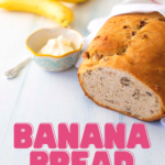 The finished banana bread sits on a table next to a few bananas and a bowl of cream cheese.