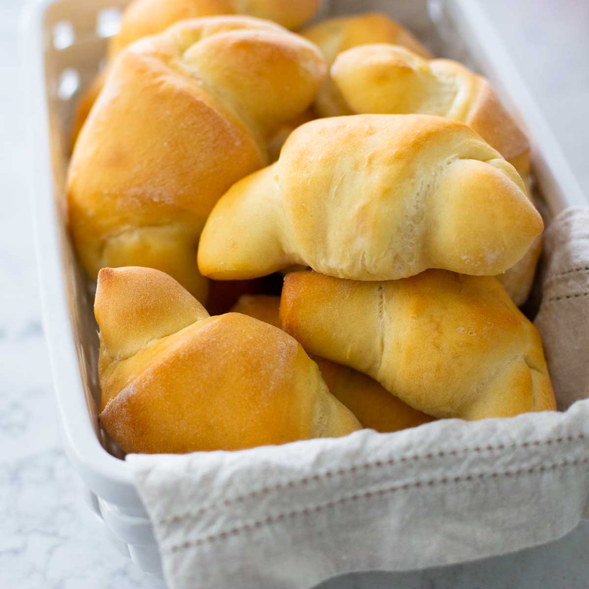 A bread basket filled with golden brown horn-shaped dinner rolls made in a bread machine.