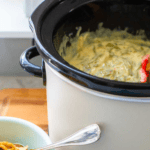 A Crockpot filled with green bean casserole sits next to a small bowl of crispy fried onions for topping.