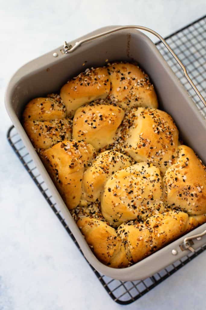 The baked Everything but the Bagel Bread sits in a bread machine bread pan on a wire rack.