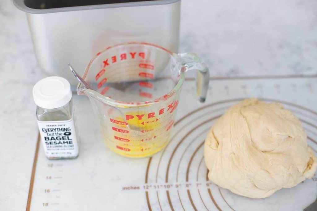 The dough sits next to a cup of melted butter and a jar of everything but the bagel seasoning.