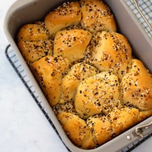 The finished everything bagel bread sits in the bread machine bread pan on a wire rack.