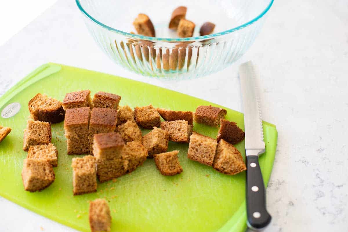 Squares of sliced brown bread sit on a cutting board next to a serrated knife.