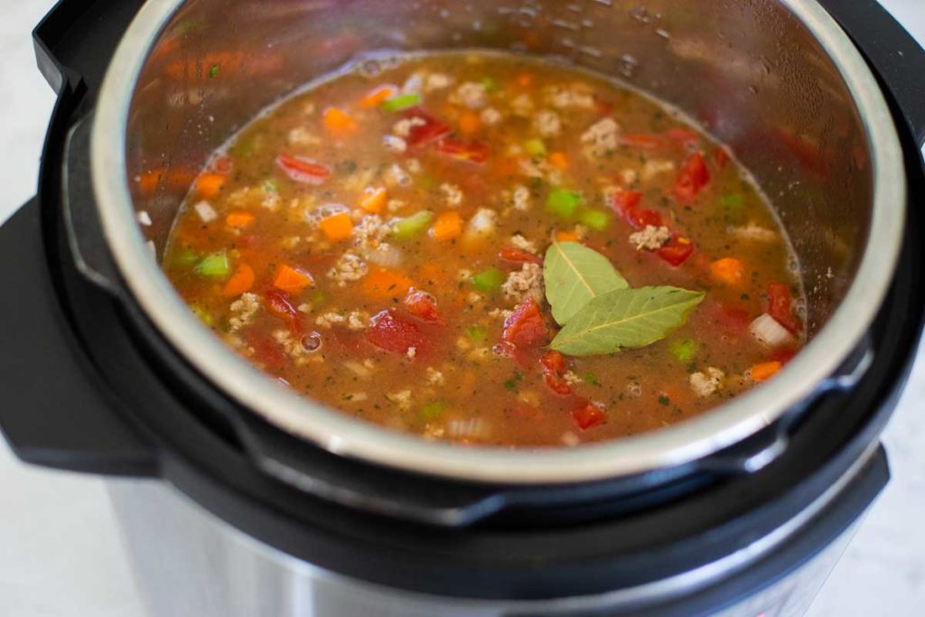 All the ingredients are now in the Instant Pot, a pair of bay leaves float on top of the beef broth and all the chopped veggies can be seen.