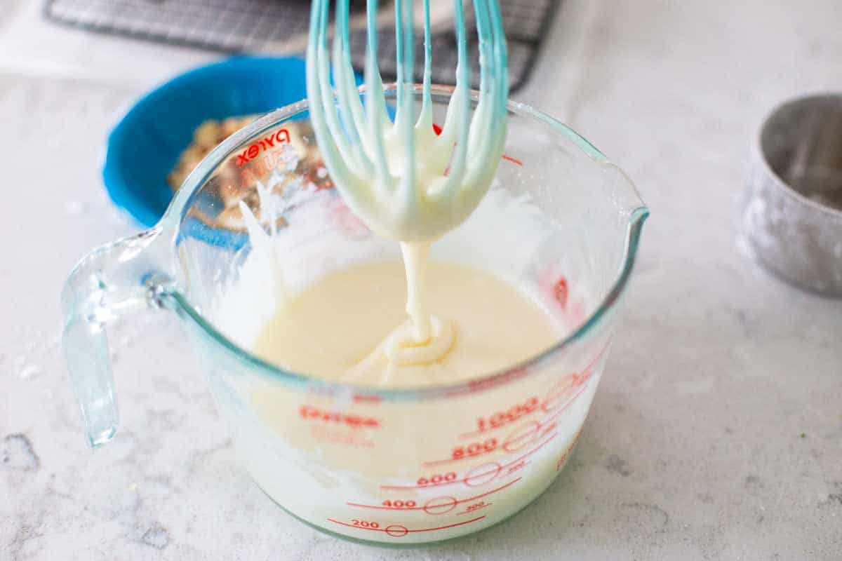 A whisk is pulling up some of the whisked glaze to show the proper consistency.