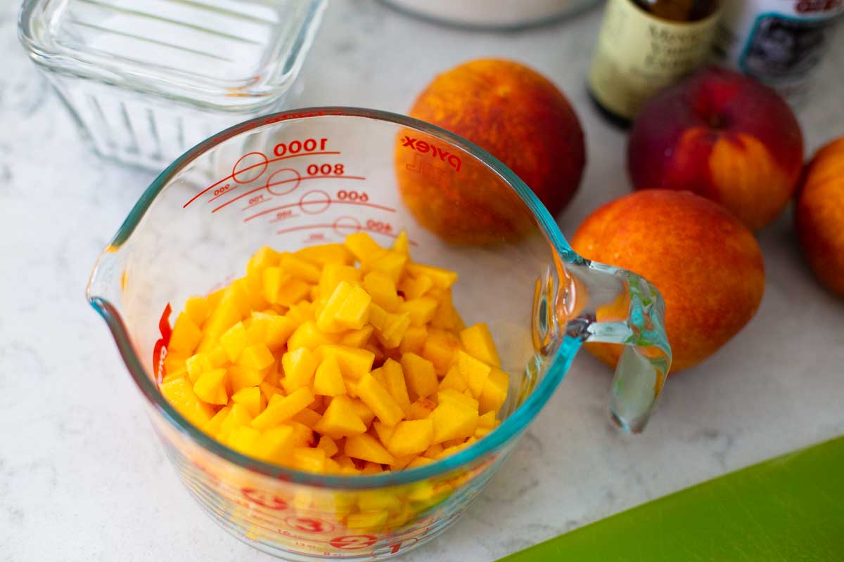 A measuring cup has diced fresh peaches to show a relative size on how to chop them.