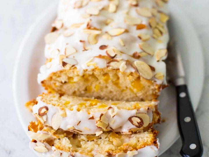 The baked peach bread with almond glaze and toasted almond slivers has been sliced so you can see the fresh peaches inside.