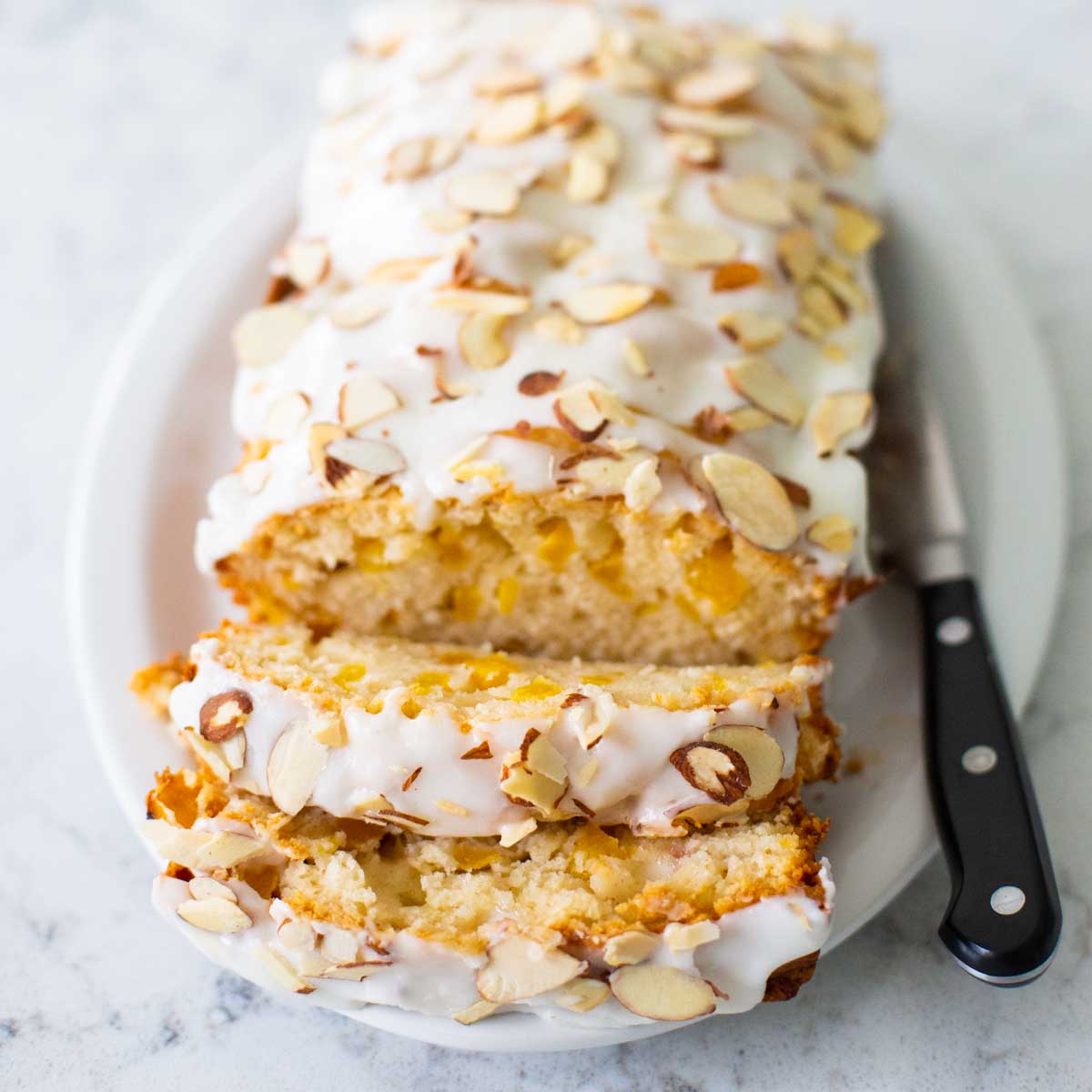 The baked peach bread with almond glaze and toasted almond slivers has been sliced so you can see the fresh peaches inside.