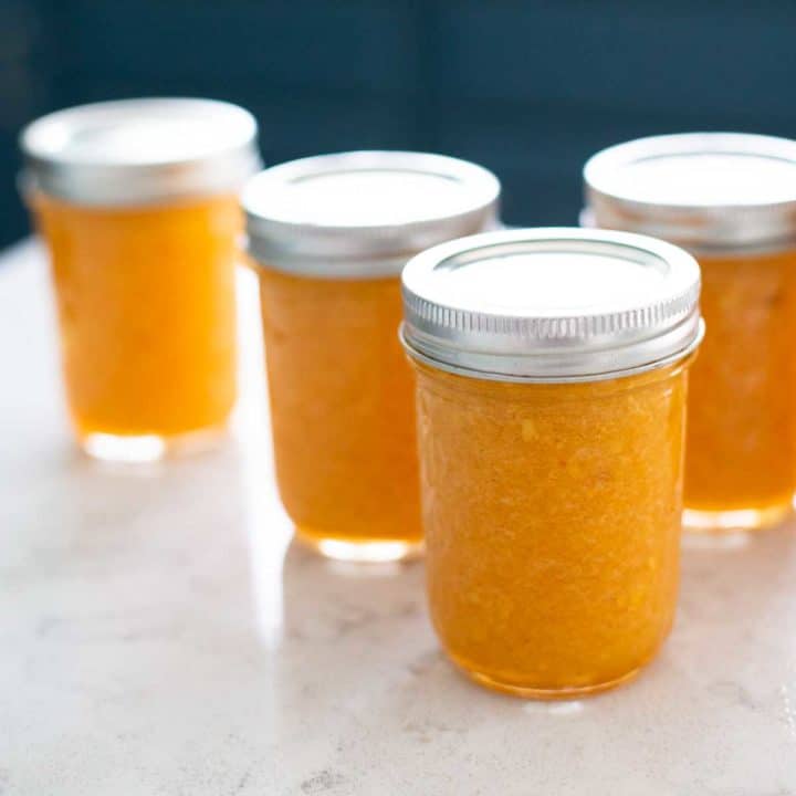 Several mason jars filled with bright orange peach freezer jam with metal lids.