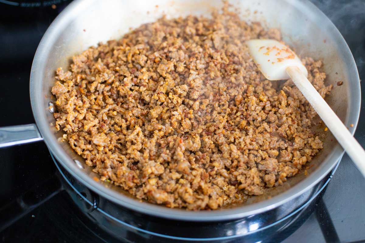 A large skillet is filled with sausage being crumbled and browned.