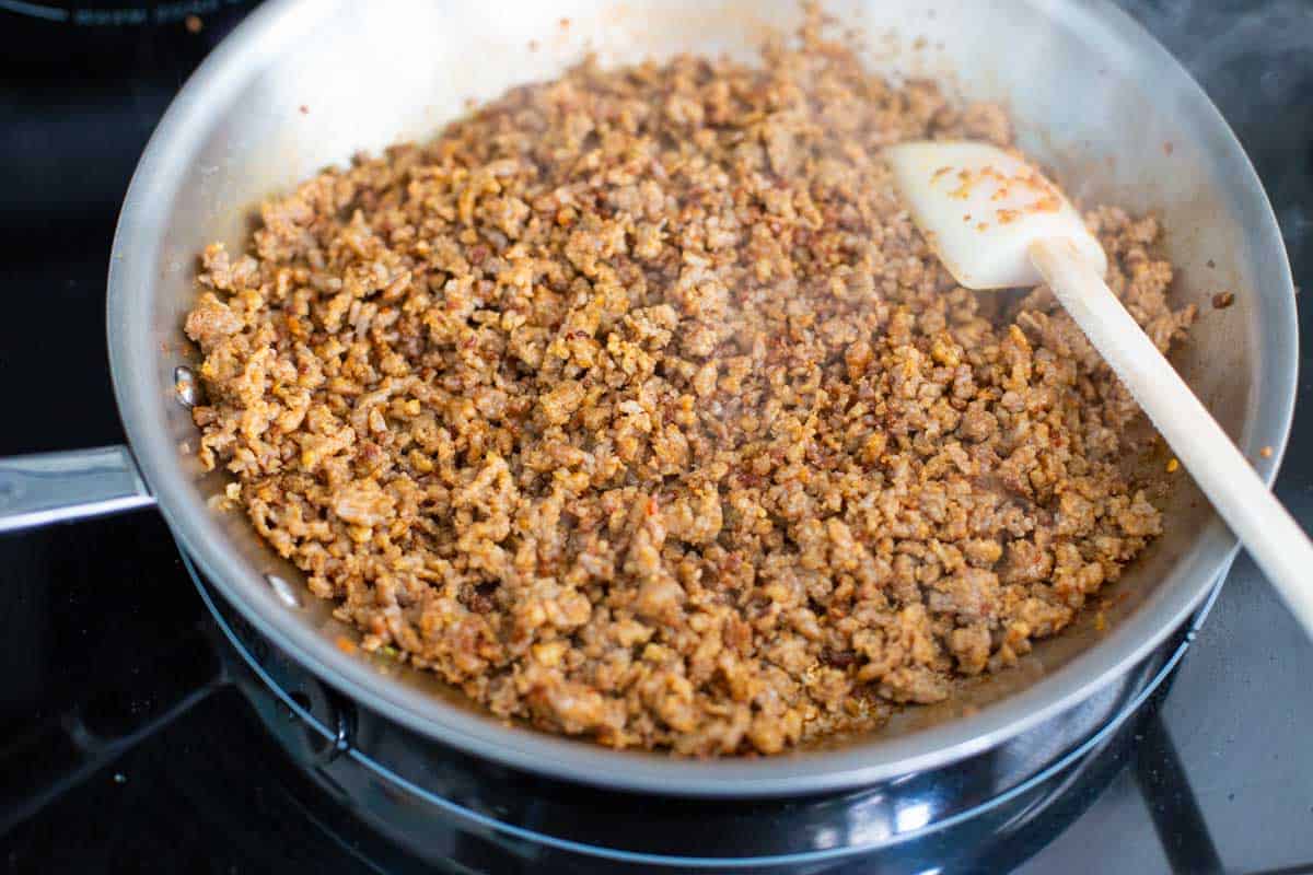 A large skillet is filled with sausage being crumbled and browned.