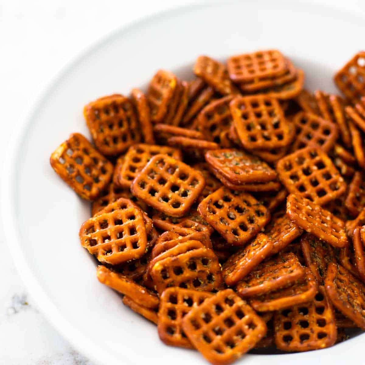 A serving bowl of square pretzels that have been baked and seasoned.