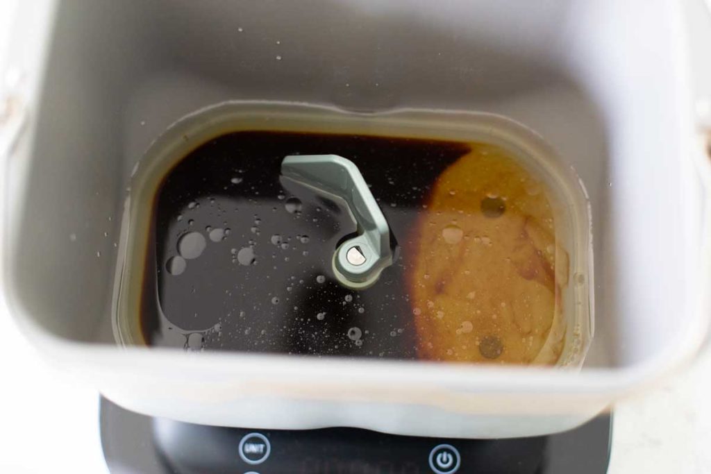 The wet ingredients for the brown bread have been put in the bottom of the bread machine bread pan with the paddle attachment.