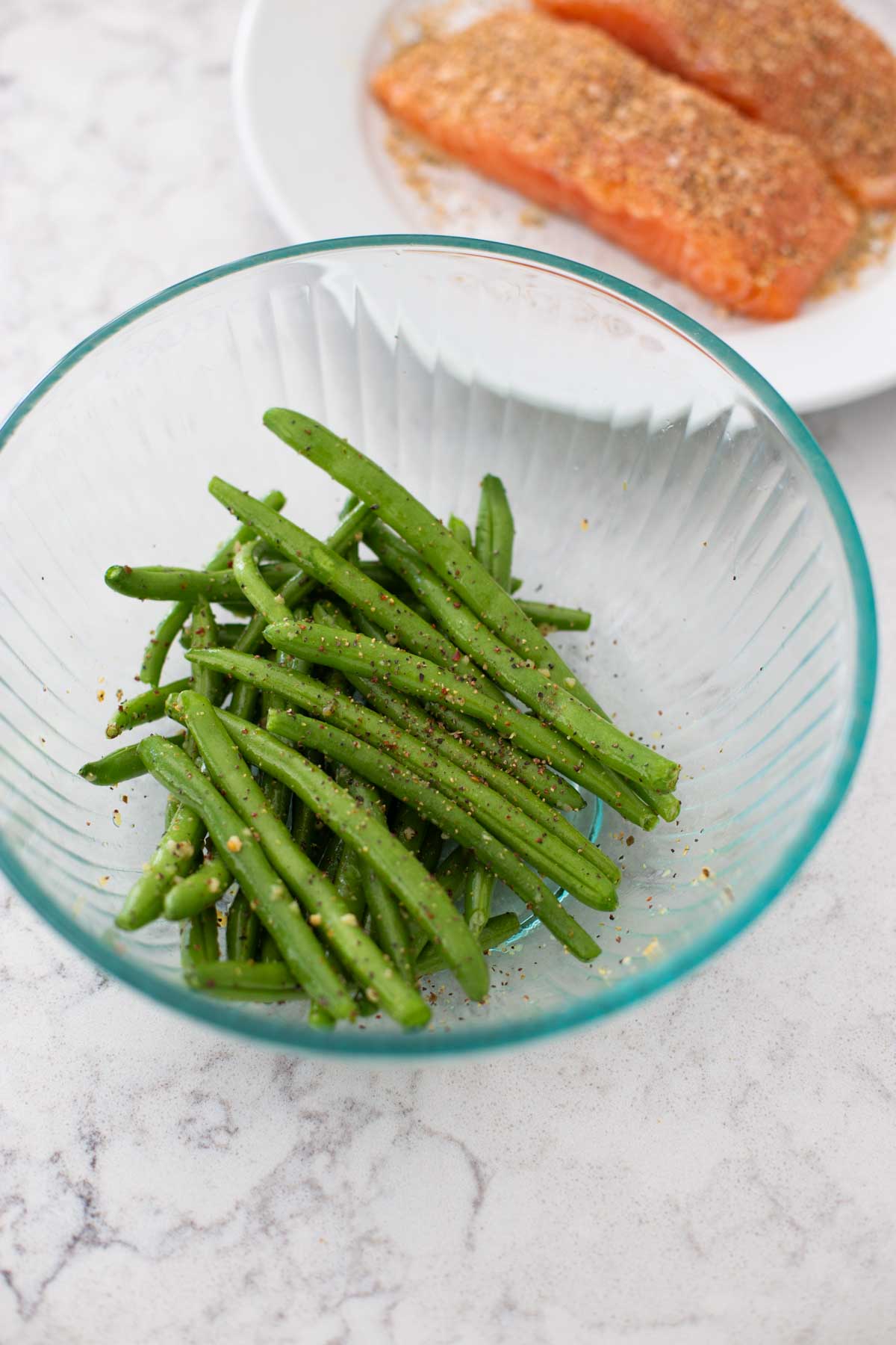 A bowl of green beans has been drizzled with olive oil and seasonings.