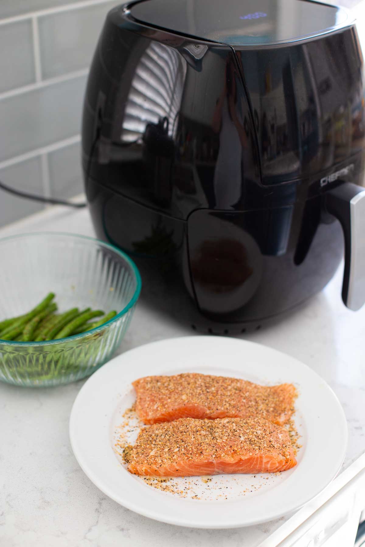 The salmon and prepared green beans are sitting next to the air fryer.