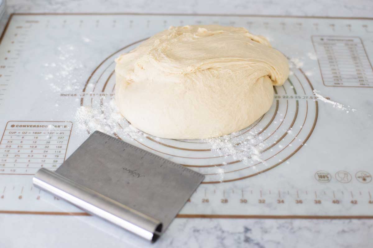 The dough has been turned out onto a baking mat. A pastry scraper sits next to it.