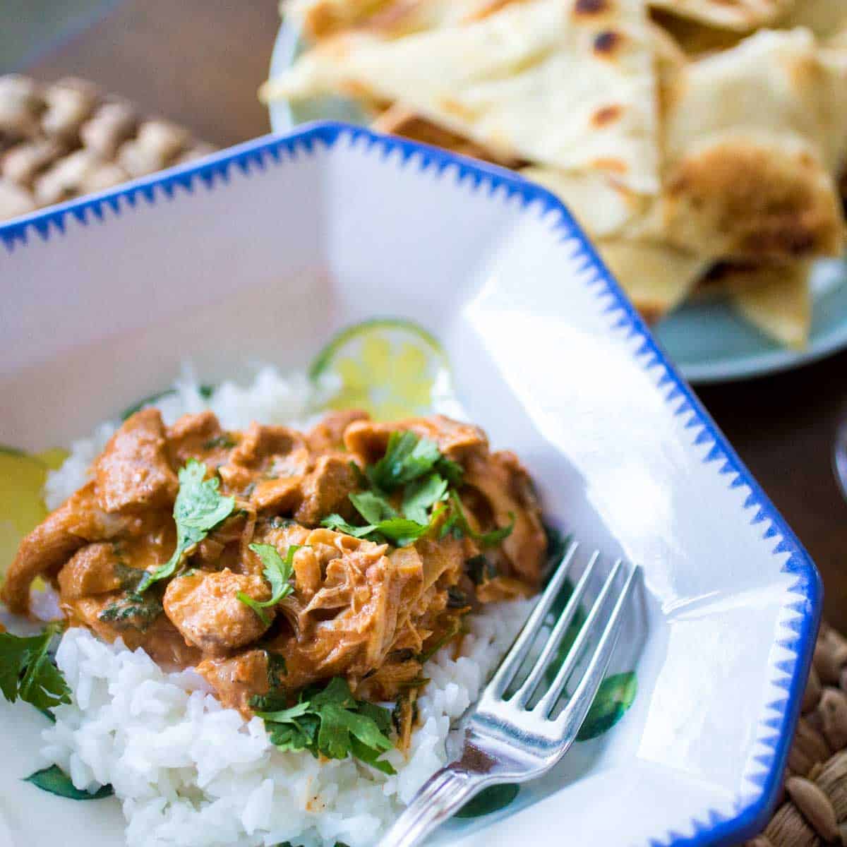 A dinner bowl has a serving of butter chicken spooned over jasmine rice. Fresh cilantro is sprinkled over the top.