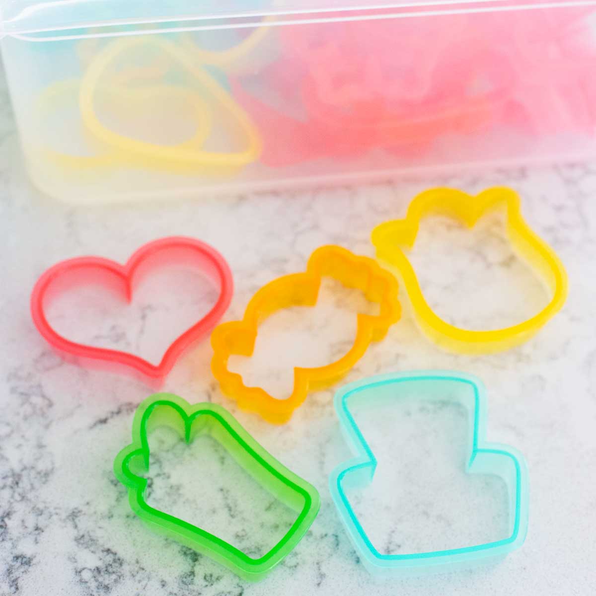 A bin of colorful sugar cookie cutters with a few samples laid out in front.
