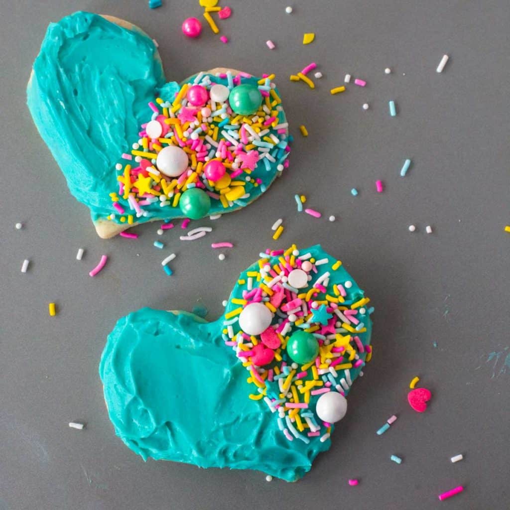 Two Heart Cookies with Blue Frosting are decorated with sprinkles on half of the cookie.