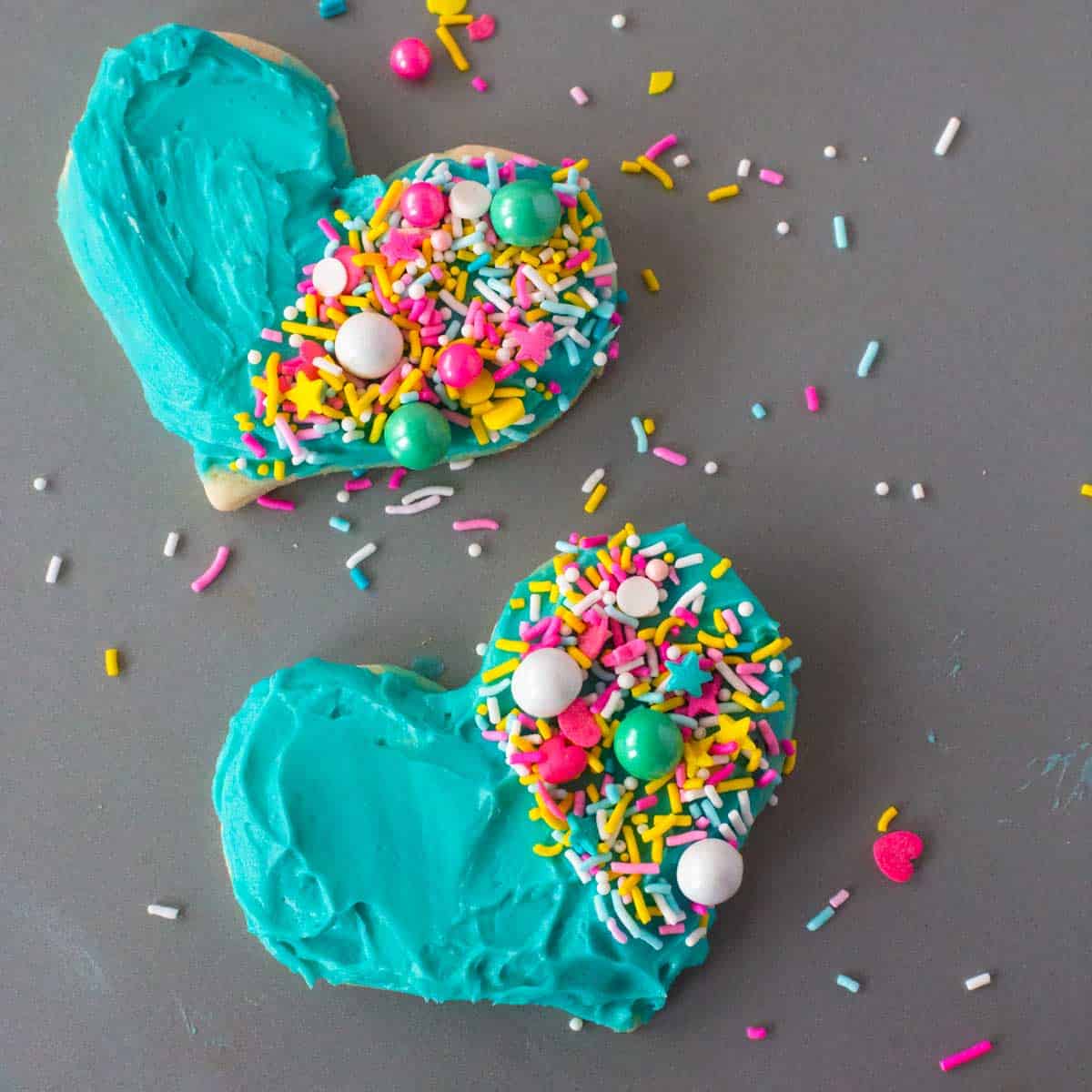 Two Heart Cookies with Blue Frosting are decorated with sprinkles on half of the cookie.