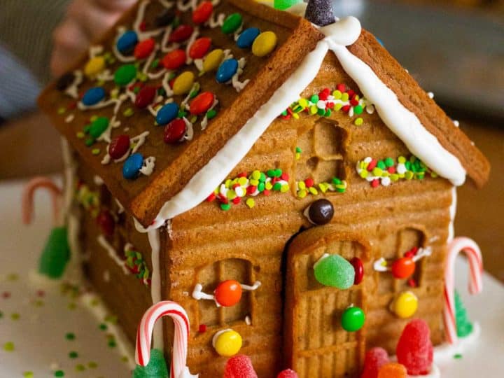 The finished gingerbread house has been assembled and decorated by a young girl with gumdrops, candy canes, and sprinkles.