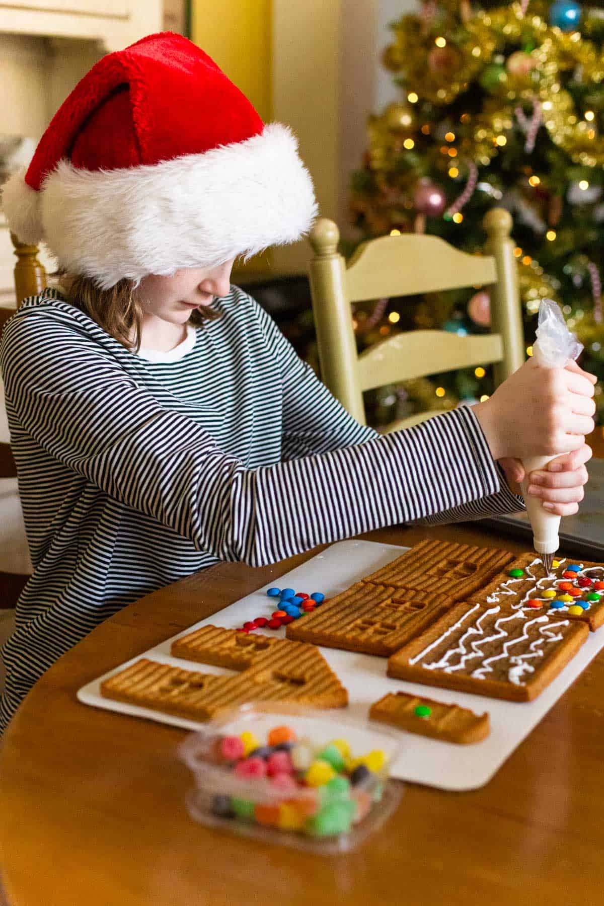 A young girl decorates the roof of her homemade gingerbread house.