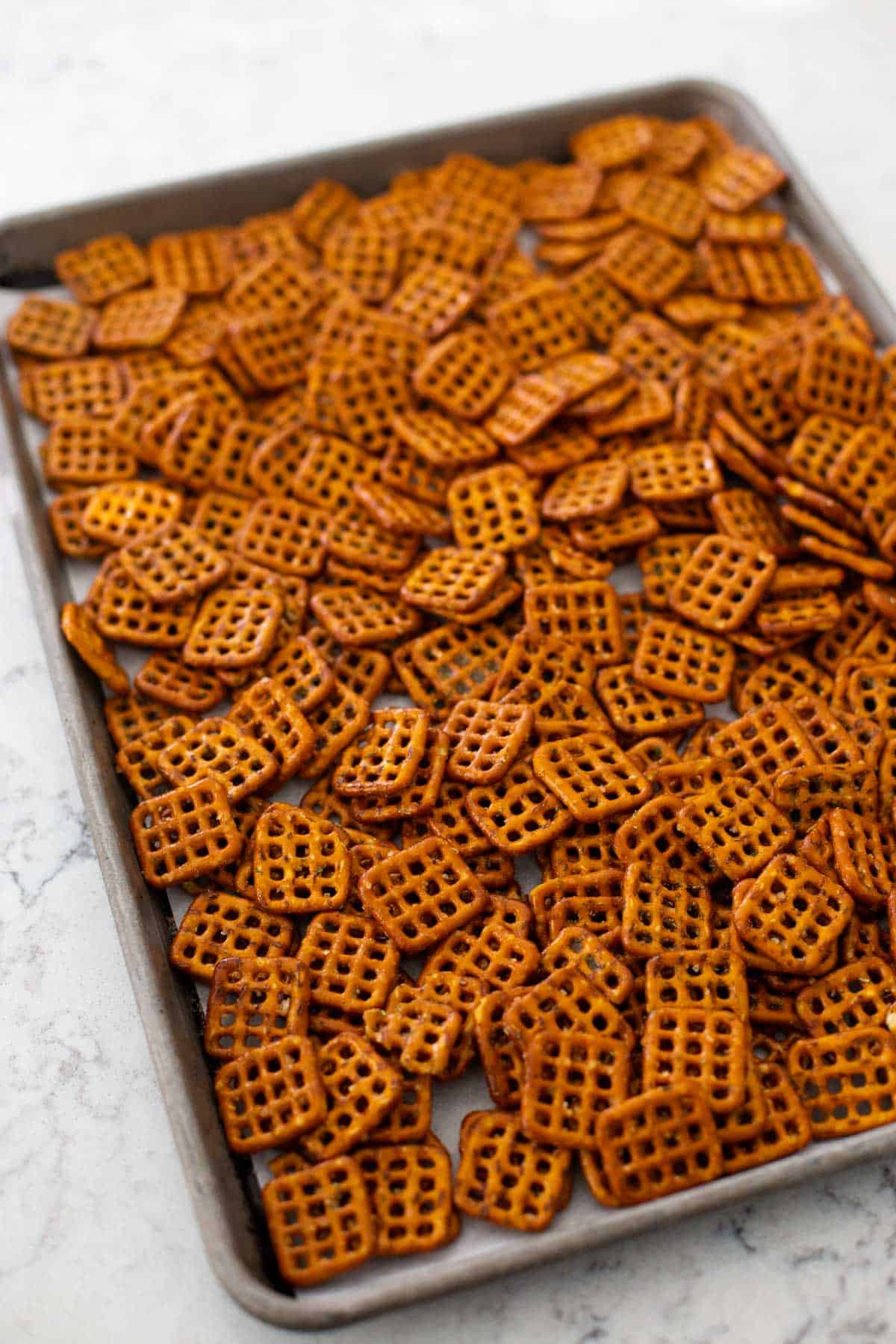 The seasoned pretzels have been spread evenly on a large baking pan and are about to be put in the oven.