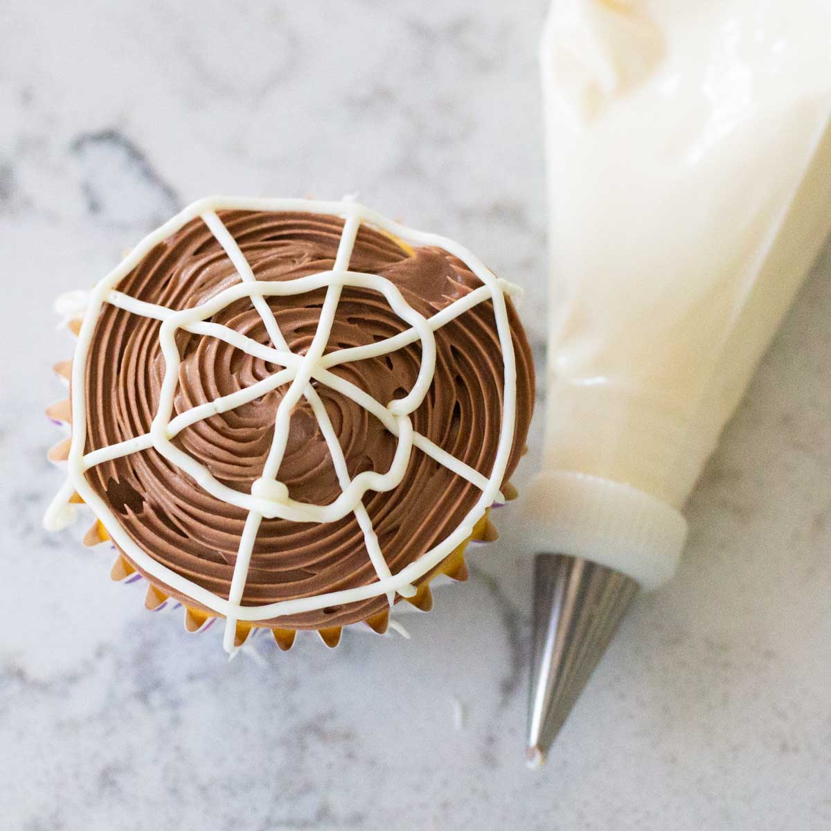 An easy spiderweb cupcake for Halloween next to a piping bag filled with frosting.